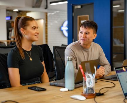 Two people sitting at a desk in a meeting smiling